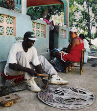 Haitian artist carving oil drum with hammer & chisel